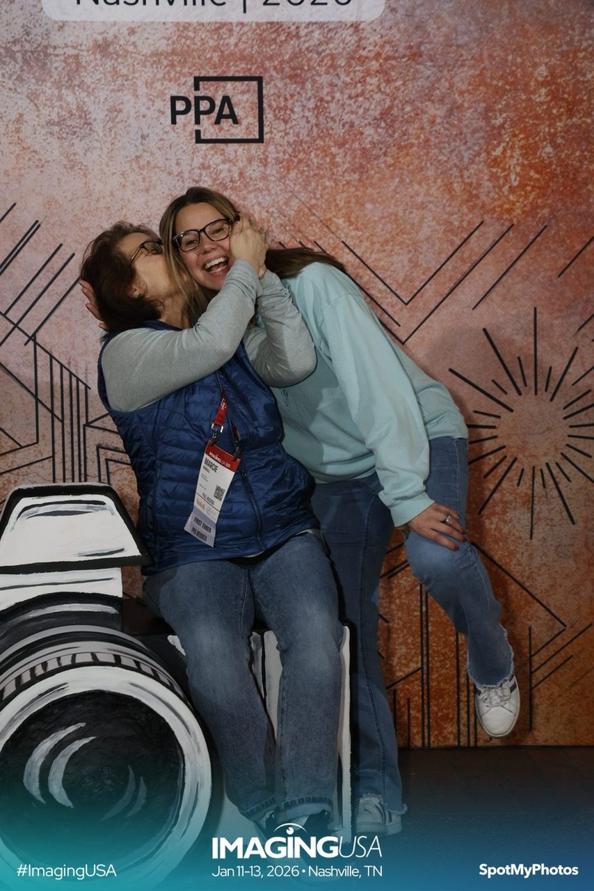 Author is hugging and kissing her friend on the cheek and they are both laughing. Posing at a photographers conference.